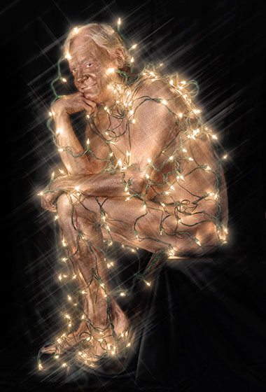 Bronze painted man posed as Rodin's Thinker and draped in holiday lights